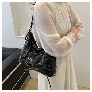 Detail of black PU tote bag featuring soft pleats, bow ribbon, and silver chain strap