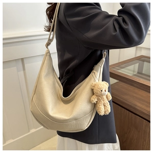 Detail of off-white crescent underarm bag with cute plush bear charm and adjustable strap