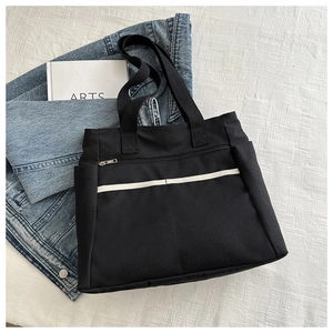 Dettaglio borsa tote in tela nera con cinturino bianco su tessuto bianco strutturato