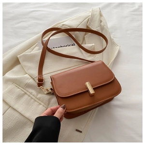 Detail of a brown leather crossbody bag with a gold metal clasp on a cream blazer