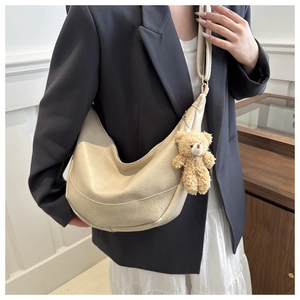 Detail view of cream crescent bag with soft pleated texture and plush bear charm