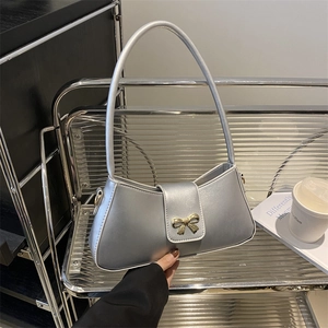 Sac baguette argenté minimaliste avec boucle noeud doré sur une étagère moderne