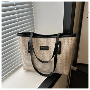 Close-up of beige woven tote bag featuring black leather trim and rectangular logo patch