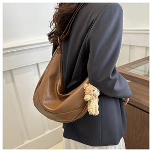 Detailed side view of a brown leather crescent shoulder bag with a plush bear charm