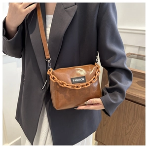 Close-up of brown glossy leather crossbody bag with chunky chain strap on a model