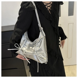 Close-up of metallic silver tote bag with bows and chain strap worn on black dress