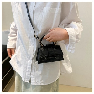Detailed view of a black crocodile pattern crossbody bag on a model wearing white