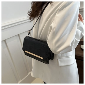 Detail of black crocodile texture leather crossbody bag with gold metal trim accent