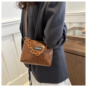 Détail d'un sac bandoulière marron rétro avec chaîne acrylique et écusson Fashion sur cuir PU