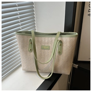 Detailed weave of beige straw tote bag with green faux leather handles and logo plaque