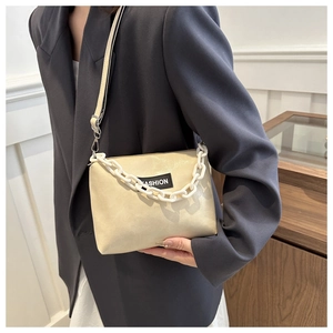 Détail d'un sac bandoulière en cuir beige avec écusson FASHION et chaîne plastique