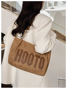 Détail d'un sac porté épaule en daim marron avec chaîne dorée sur un blazer blanc