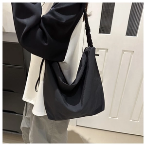 Detail of black wrinkled nylon tote bag showing woven shoulder strap and zipper closure