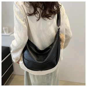 Detail of black pleated hobo bag with a plush bear charm worn by a model