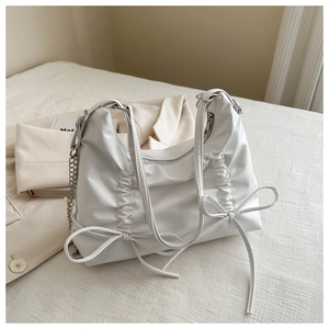 Close-up of white ruched backpack with bow detail and metallic chain strap accents