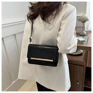 Detail of black crocodile pattern crossbody bag with gold metal trim on elegant model