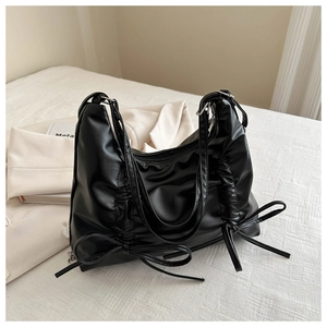 Close-up of black pleated PU leather shoulder bag with decorative bow ties and zipper