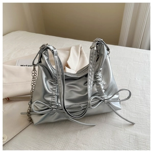 Detail of silver metallic tote bag with bow accents and pleated texture on white surface