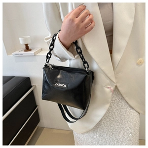 Detail of a black crossbody bag with chunky chain handle and fashion label tag