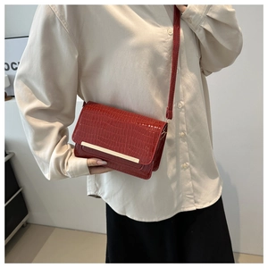 Detail of red crocodile pattern crossbody bag with elegant gold metal trim on flap