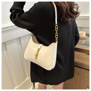 Detail of a cream-colored leather baguette bag featuring a gold buckle and chain strap
