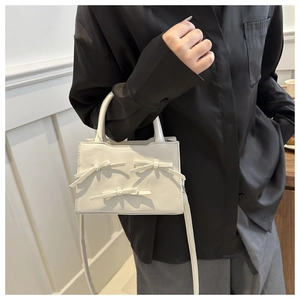 Dettaglio mini borsa a tracolla bianco crema con tre eleganti fiocchi di perle su pelle opaca