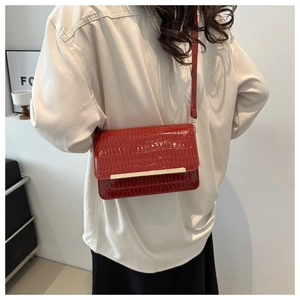 Close-up of red crocodile pattern crossbody bag with gold buckle on a fashion model