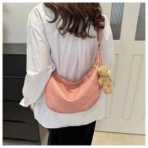 Pink crescent shoulder bag with plush bear charm worn by model in a home setting