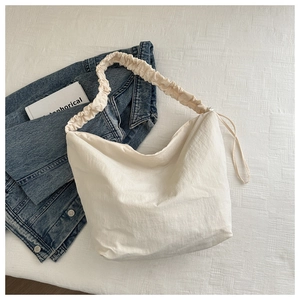 Close-up of large beige canvas tote bag with pleated cloud strap on plaid bedding