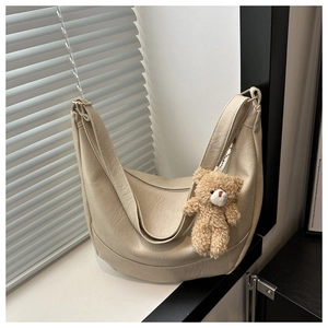 Detail of cream hobo tote bag with a brown plush bear keychain on a sunny windowsill