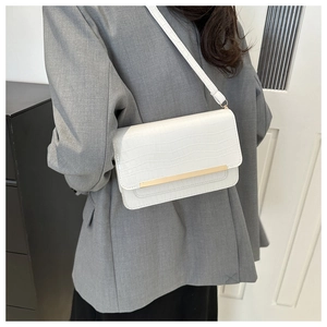 Detail of white crocodile pattern crossbody bag featuring a sleek gold metal bar buckle
