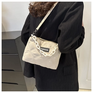 Dettaglio borsa a tracolla trapuntata beige con etichetta moda e catena decorativa bianca