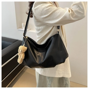 Detail of black matte PU leather hobo bag with fashion logo and brown plush bear charm