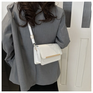 Detail of white crocodile-textured square bag with gold bar accent and adjustable strap