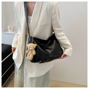 Detail of black faux leather hobo tote bag with cute beige teddy bear charm on shoulder