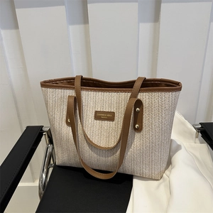 Grand sac cabas en paille à motif chevrons et anses en cuir marron sur une chaise noire