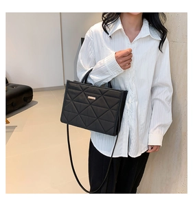 Close-up of black quilted shoulder bag featuring elegant diamond stitching and metal plaque