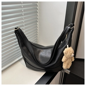 Detail of black crescent shoulder bag with glossy finish and cute plush bear charm decoration