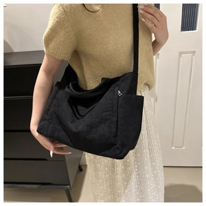 Detail of black corduroy tote bag with side zipper pocket shown on a shoulder