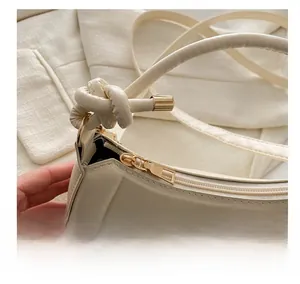Detailed close-up of smooth zipper and knotted strap design on cream leather shoulder bag