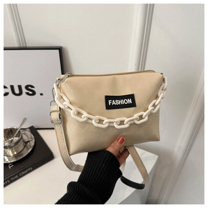 Detail of a cream textured leather shoulder bag with a bold white acrylic chain link