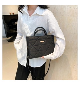 Detail of black quilted crossbody bag with gold metal plaque and dual handles for women