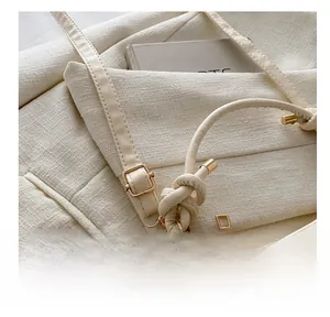 Detail of adjustable gold metal buckle and knotted leather strap on cream saddle bag