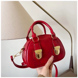 Detail of red glossy Boston bag with gold hardware and dual handles in a warm setting