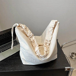 Minimalist beige drawstring tote bag with pleated design on a modern office desk