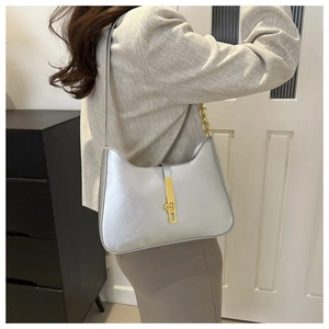 Silver faux leather crescent underarm bag with gold buckle shown on a shoulder