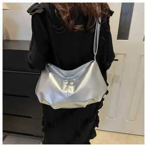 Detailed view of a silver metallic tote bag worn over the shoulder in a modern room