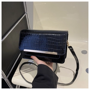 Detail of crocodile pattern small square bag with golden metal bar and long shoulder strap