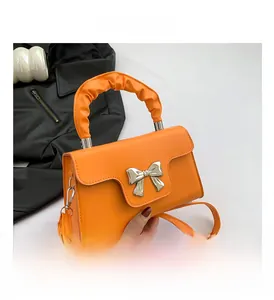 Detail of mini orange square bag featuring a metal bow accent and ruffled handle texture
