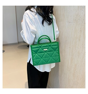 Detail of green quilted crossbody bag shown as a shoulder bag on a model in white shirt